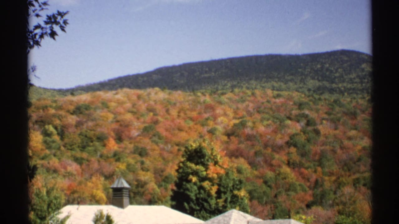 1971 New York 8mm frame showing a colorful forested hillside with a large pale roof and chimney partly visible below.