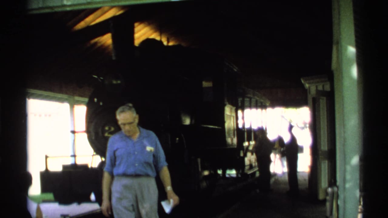 1971 New York 8mm frame of a man in a blue shirt walking through a shadowed station interior near a dark locomotive.