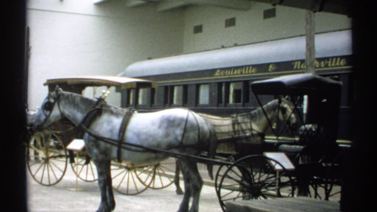 1971 New York home-movie frame showing a white horse and black carriage in front of a Louisville & Nashville rail car display.