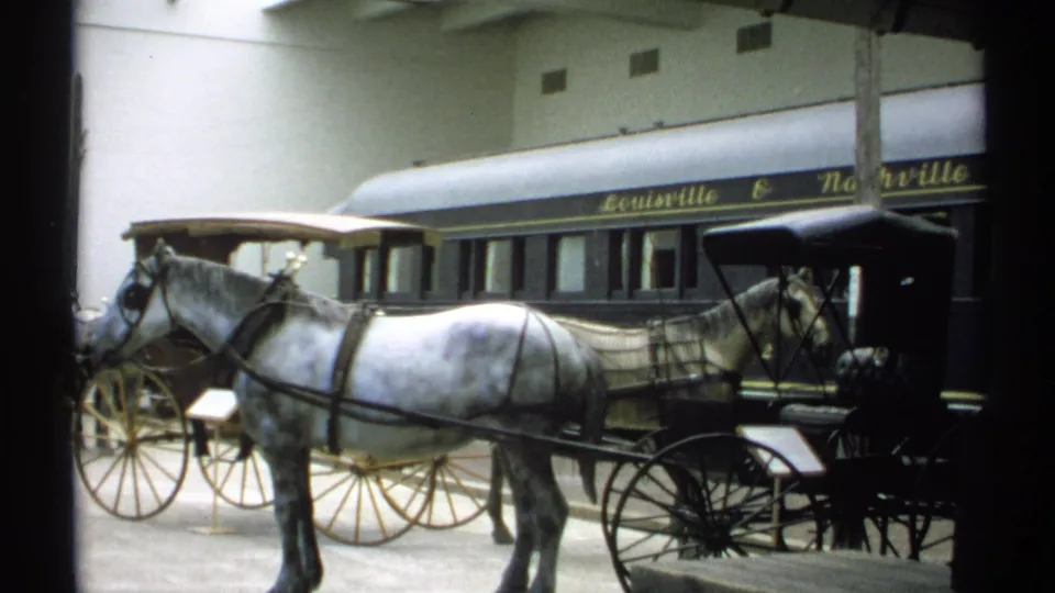 1971 New York home-movie frame showing a white horse and black carriage in front of a Louisville & Nashville rail car display.