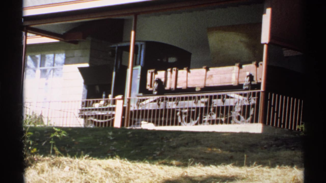 Handheld 1971 New York frame showing the rail car display from a low visitor angle, with grass, railing, and building details visible.