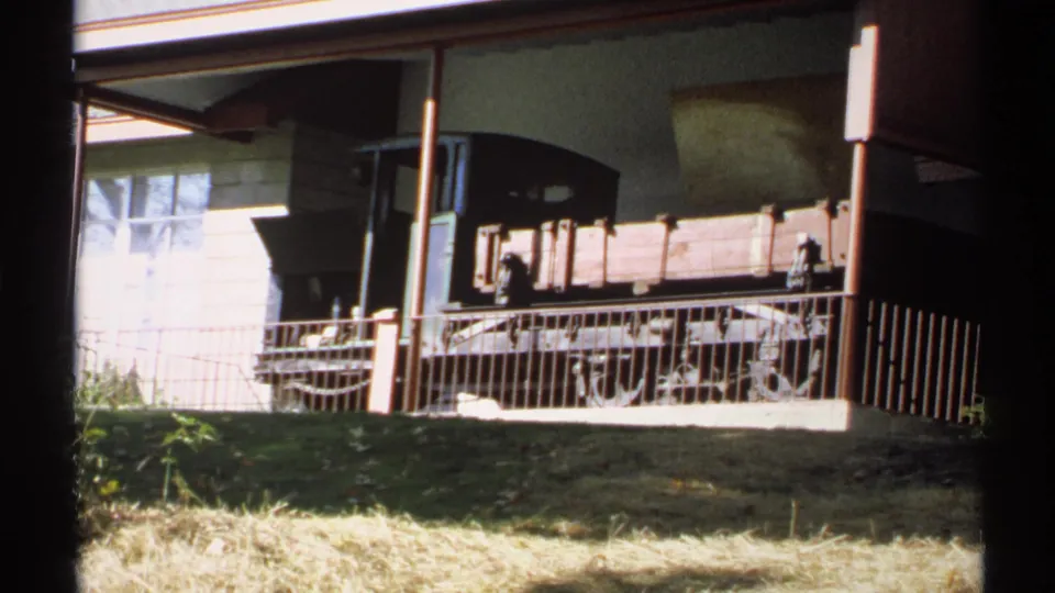 Handheld 1971 New York frame showing the rail car display from a low visitor angle, with grass, railing, and building details visible.