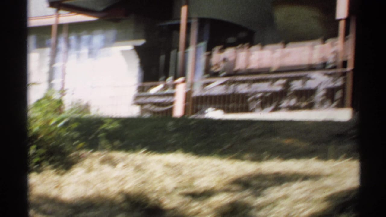 Soft, motion-blurred 1971 New York home-movie frame of the historic rail car exhibit behind a railing in bright daylight.