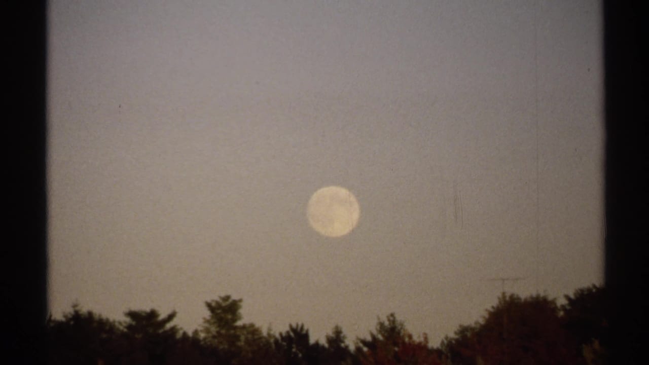 1971 New York 8mm frame with the moon centered over a dark treeline and muted autumn color below.