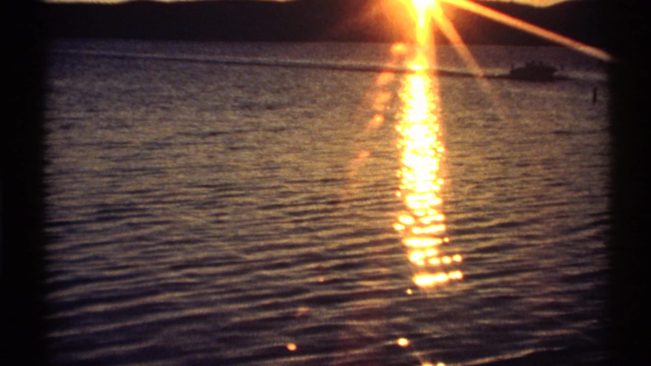 1971 New York home-movie frame showing sunset light on water and a small distant boat near the horizon.