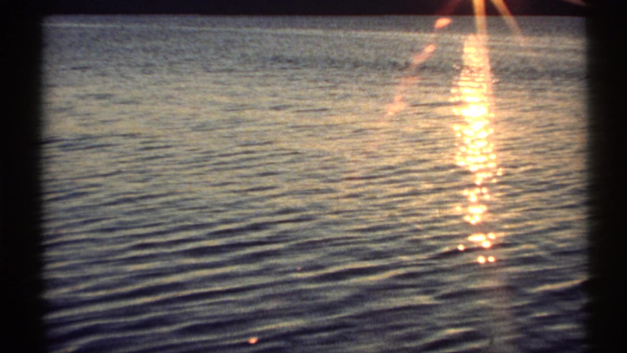 1971 New York 8mm frame showing a bright sunset reflection stretching over rippling river water.