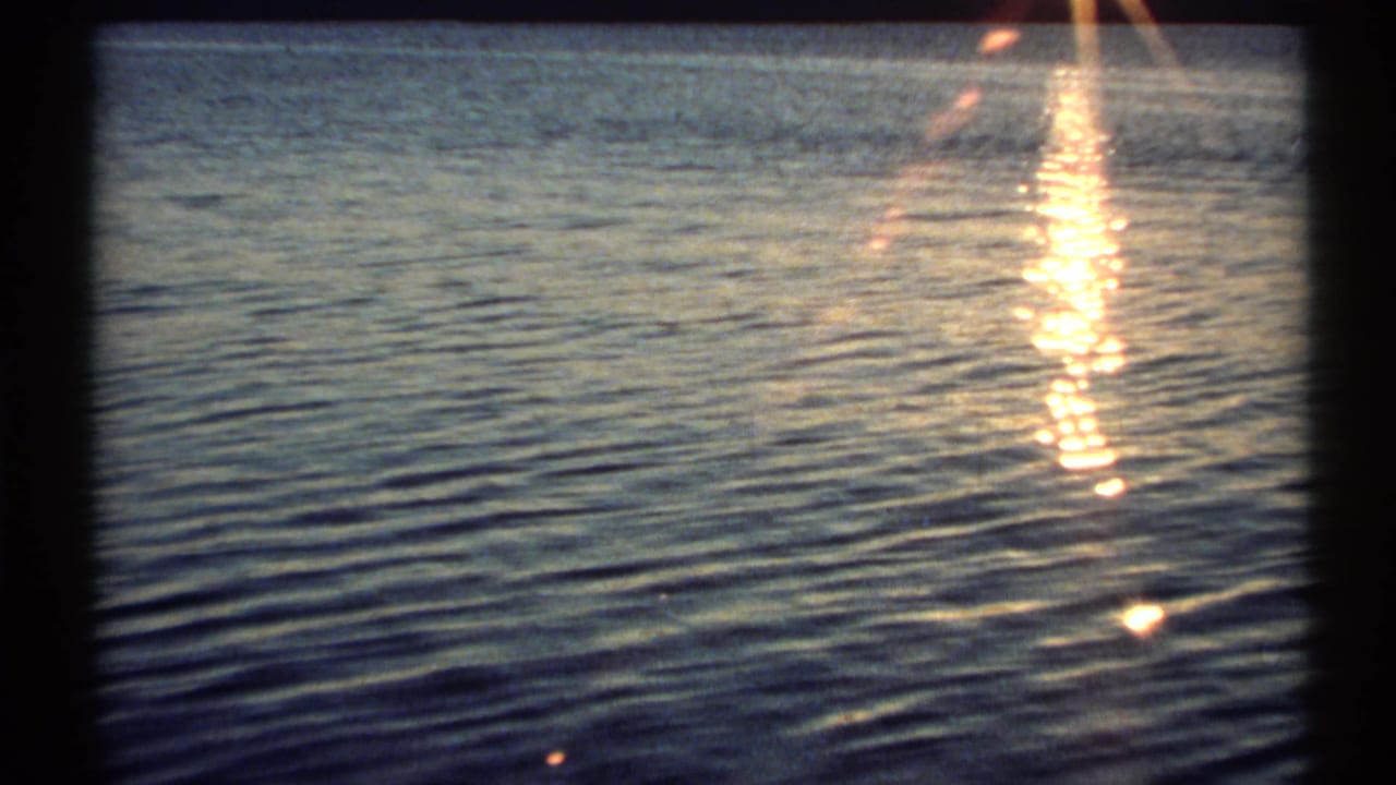 Vintage 8mm view of river water in New York, with warm sunset glare shimmering near the frame edge.