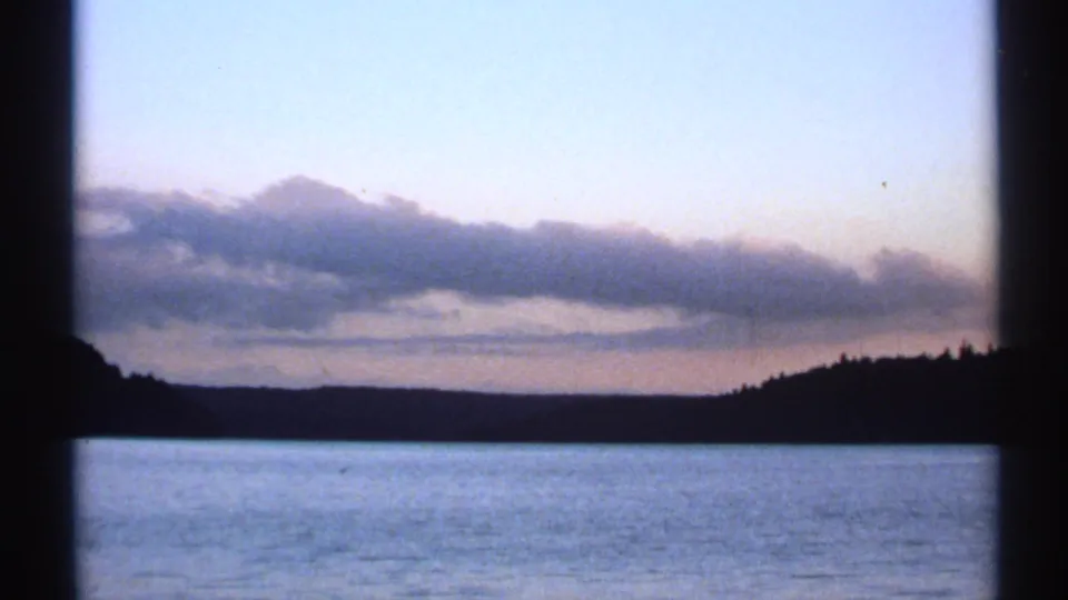 1971 New York river landscape at dusk, with a silhouetted wooded shore beneath layered clouds.