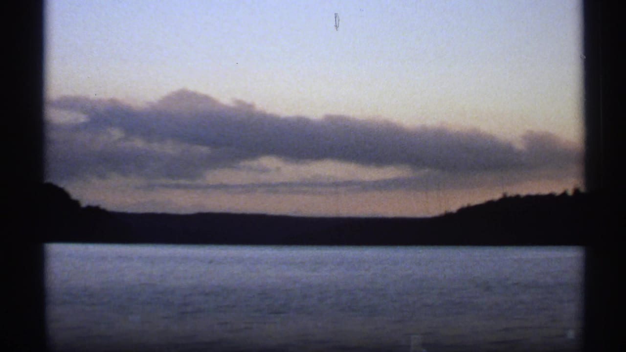 Distant wooded shore and cloud band over still water, partly blocked by window framing.