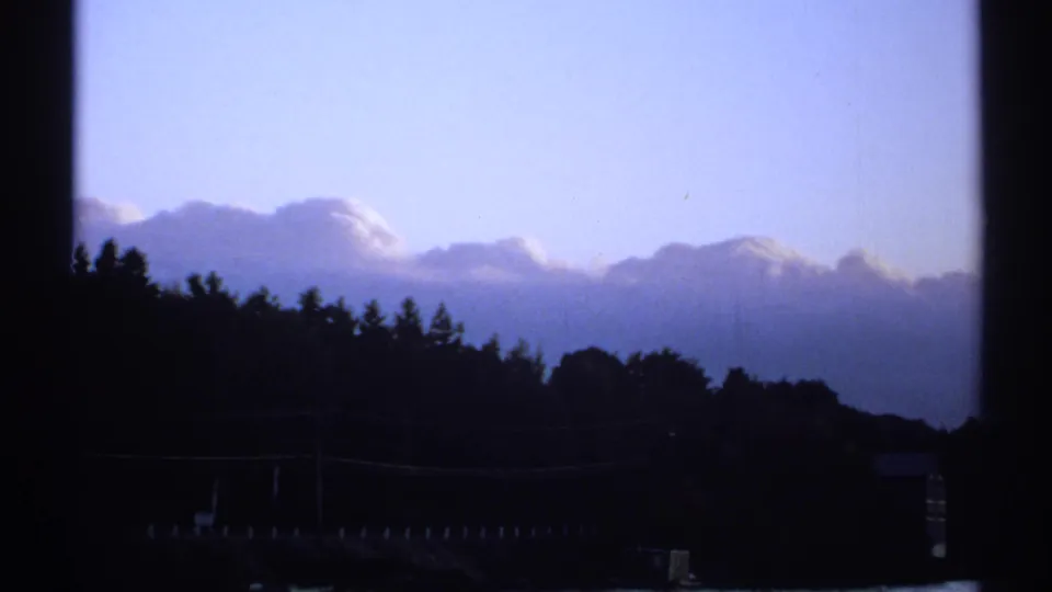 1971 New York 8mm frame with silhouetted trees, blue-purple clouds, window bars, and a faint shoreline structure near the water.