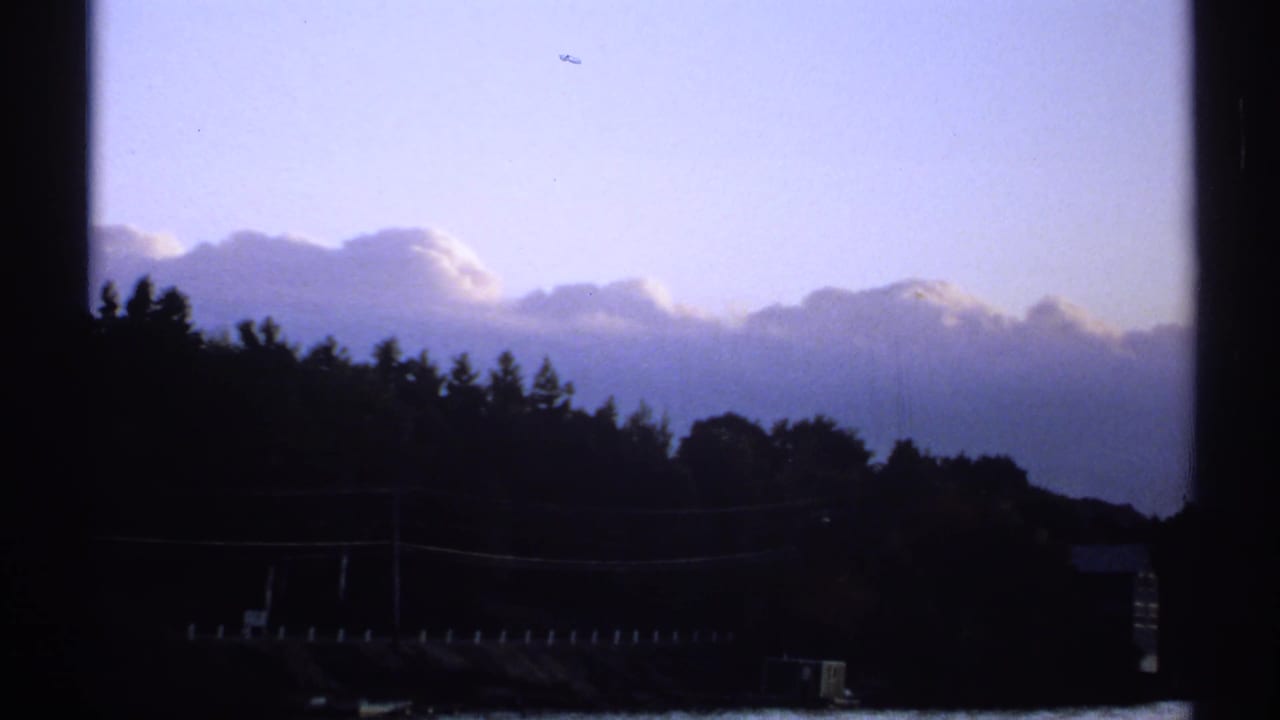 1971 New York 8mm frame showing a silhouetted treeline and low hill under layered clouds and pale blue sky.
