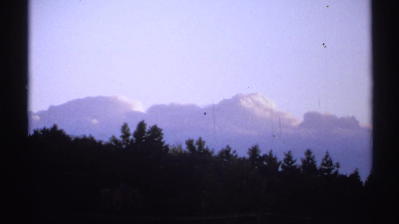 1971 New York 8mm frame with dark trees along the horizon beneath soft clouds and a blue-violet sky.