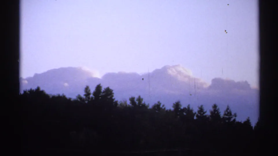 1971 New York 8mm frame with dark trees along the horizon beneath soft clouds and a blue-violet sky.