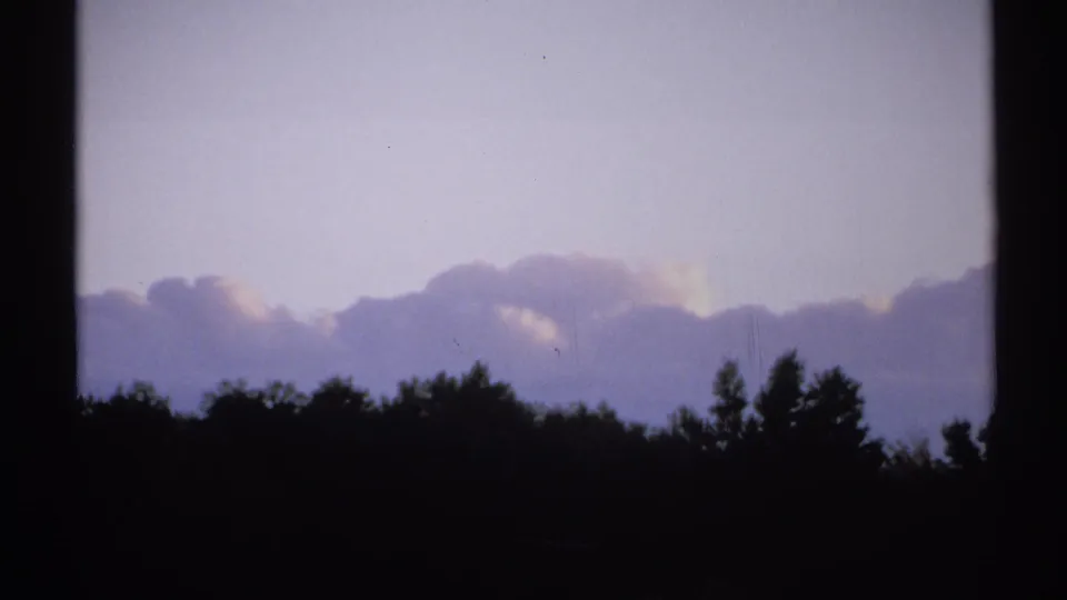1971 New York 8mm view of dark treetops against rounded clouds and a hazy purple-pink sky, bordered by heavy frame shadows.