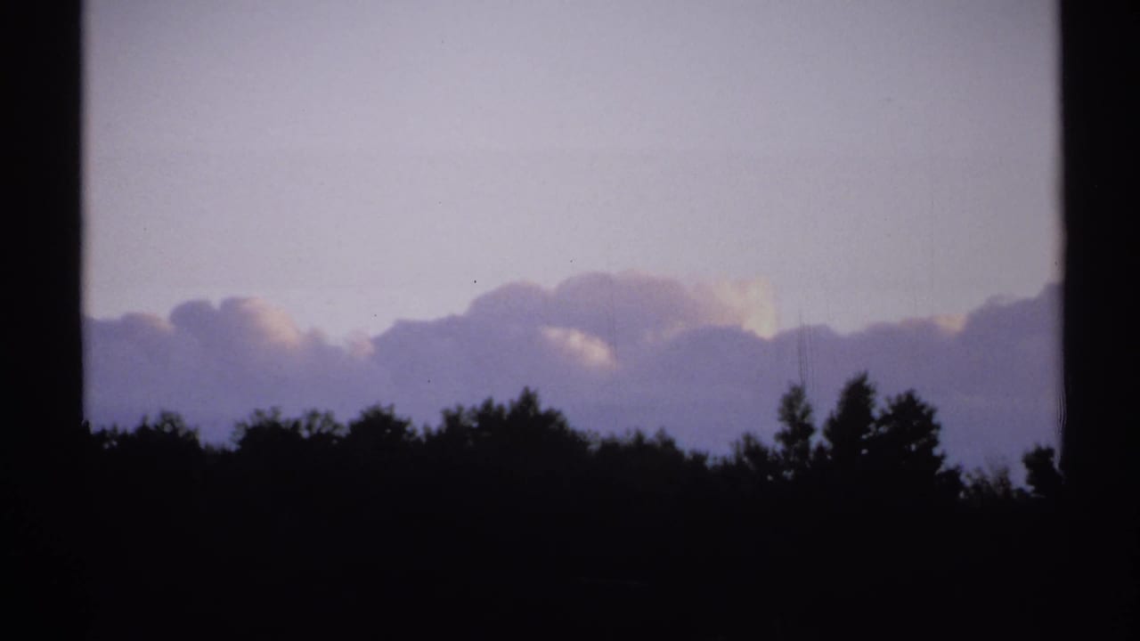 1971 New York 8mm frame with a low, dark treeline, pale clouds, and a washed lavender sky showing light film wear.