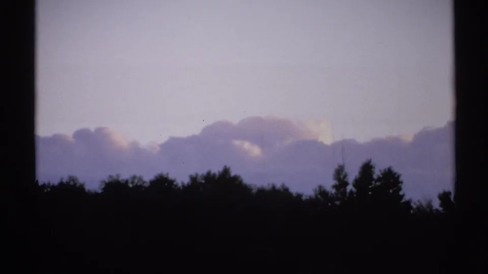 1971 New York 8mm frame with a low, dark treeline, pale clouds, and a washed lavender sky showing light film wear.