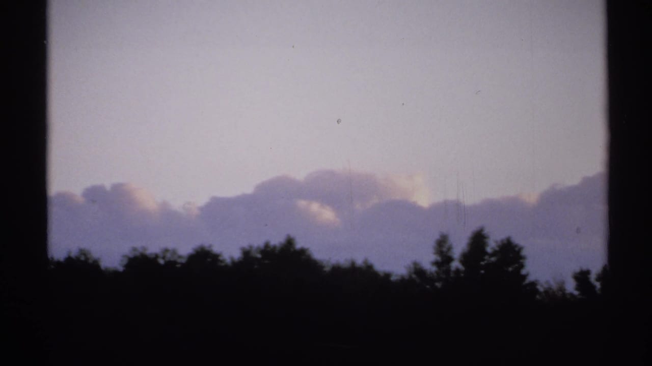 1971 New York 8mm frame showing silhouetted trees, layered clouds, and a dim purple sky through dark vertical frame divisions.