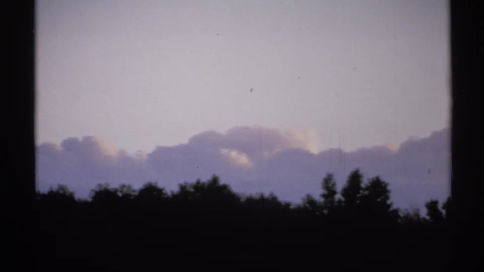1971 New York 8mm frame showing silhouetted trees, layered clouds, and a dim purple sky through dark vertical frame divisions.
