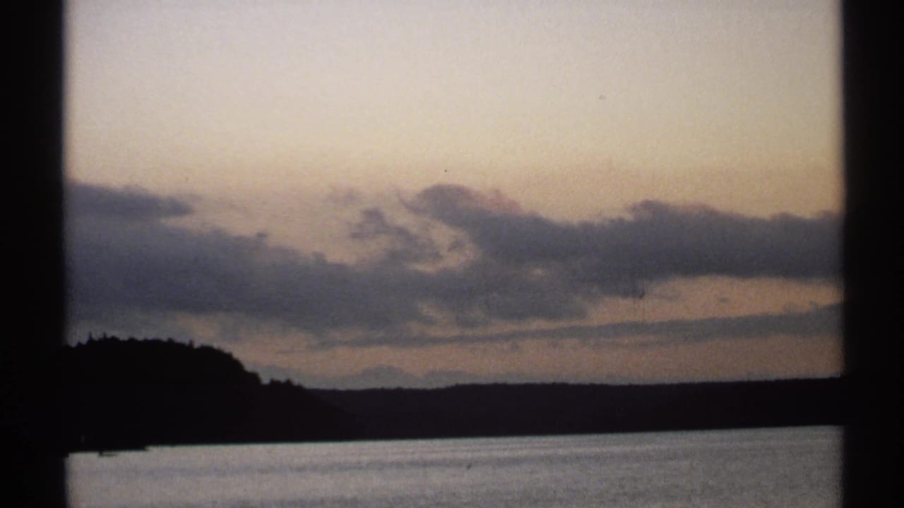 1971 New York 8mm frame with soft clouds, a dim horizon, calm water, and dark scanned film-frame dividers.