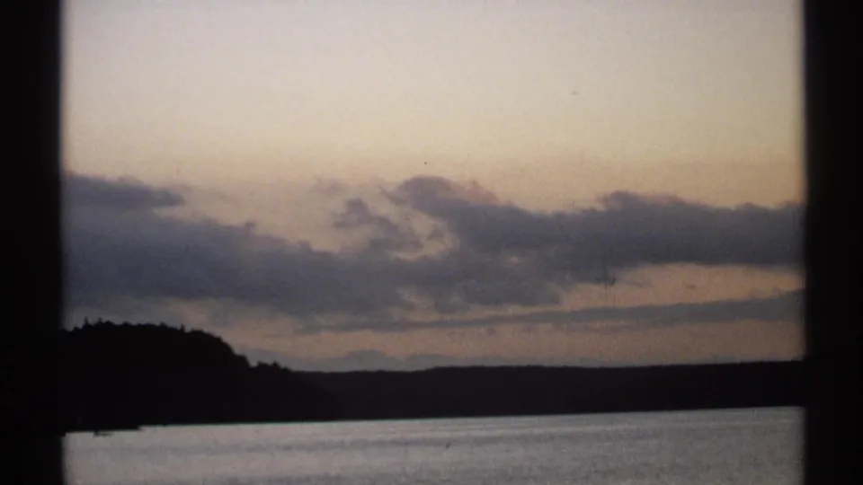 1971 New York 8mm frame with soft clouds, a dim horizon, calm water, and dark scanned film-frame dividers.
