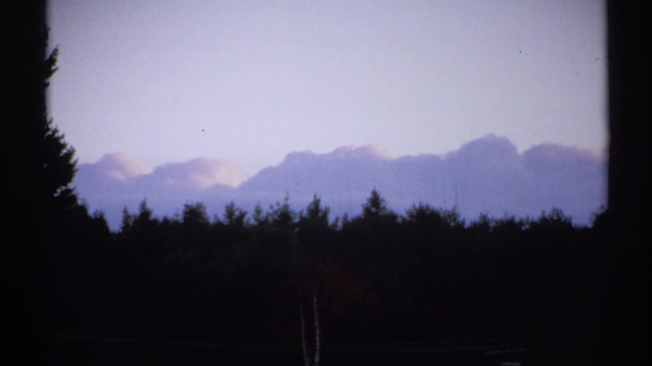 1971 New York 8mm frame with a dark wooded foreground, faint distant mountains, and a pale evening sky.