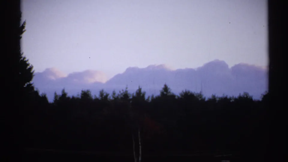1971 New York 8mm frame with a dark wooded foreground, faint distant mountains, and a pale evening sky.
