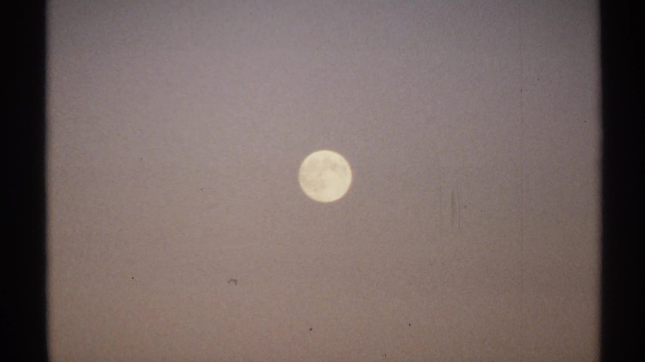 1971 New York 8mm frame showing a bright moon suspended in a hazy, lightly mottled sky.