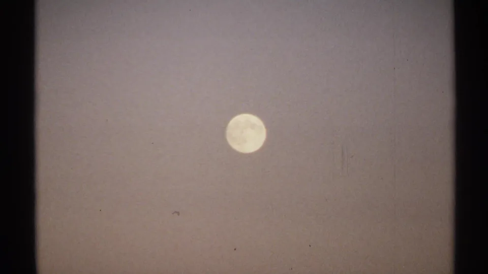 1971 New York 8mm frame showing a bright moon suspended in a hazy, lightly mottled sky.