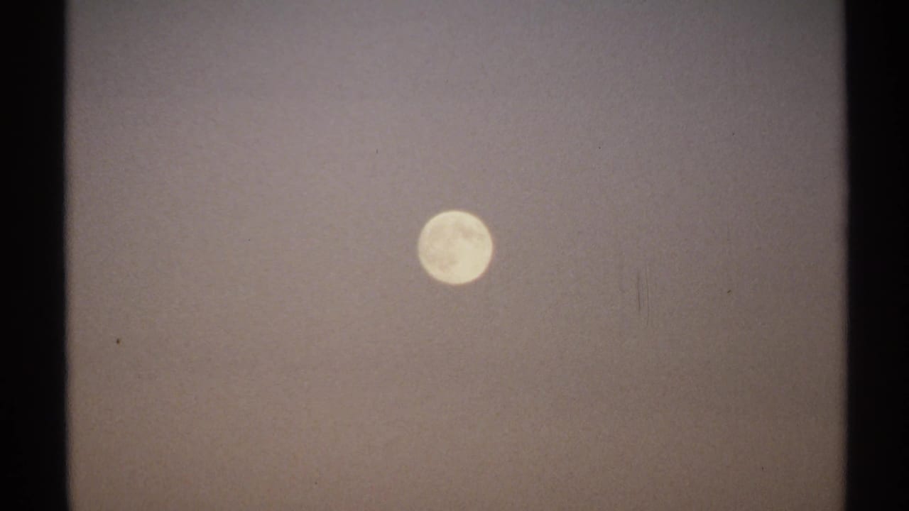 Pale full moon against a hazy gray night sky with dark film borders.