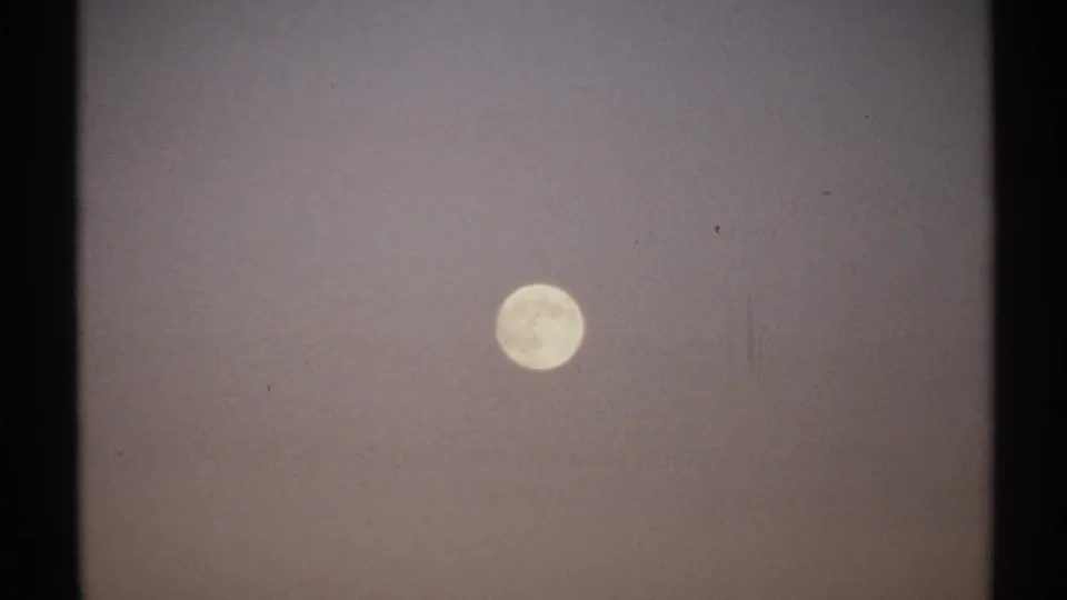 1971 8mm New York frame with the full moon held in a hazy sky, showing grain, slight softness, and contact-sheet cropping.