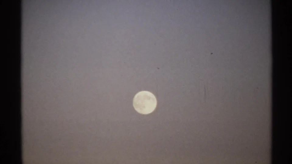 1971 8mm New York home-movie frame where the handheld camera places the full moon lower in a hazy, grainy sky.