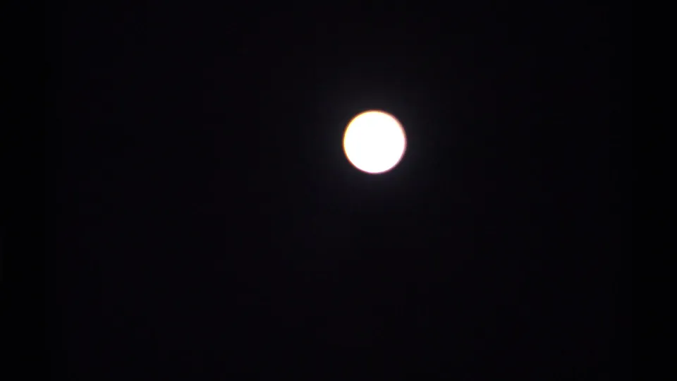 Bright full moon in a dark night sky from 1971 New York 8mm home-movie footage, with soft exposure bloom around the moon.