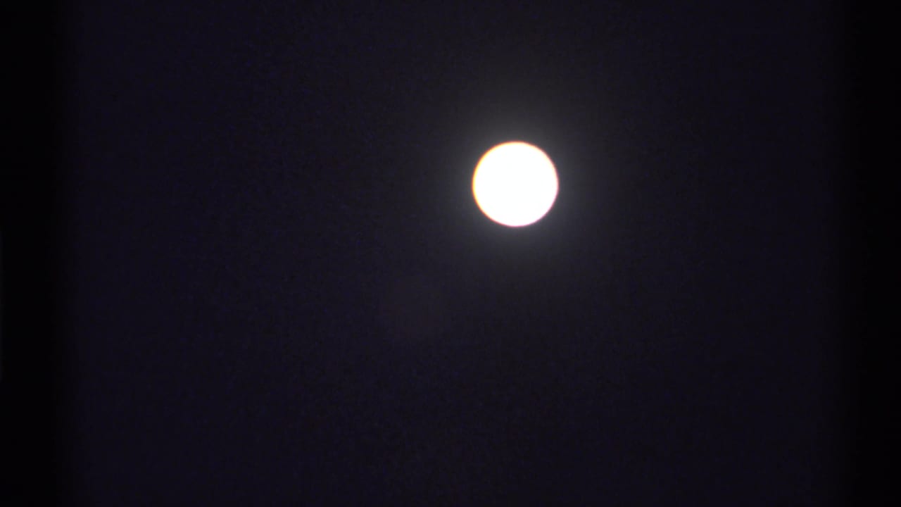 The moon appears bright and slightly overexposed in the lower part of the dark 8mm frame, with visible grain and a soft halo.