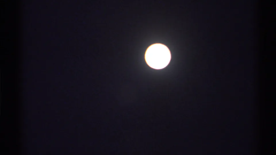 The moon appears bright and slightly overexposed in the lower part of the dark 8mm frame, with visible grain and a soft halo.
