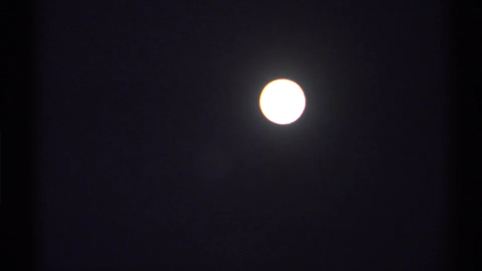 A bright full moon glows in the dark sky, with 8mm grain, mild flicker, and a small halo visible around the overexposed disc.