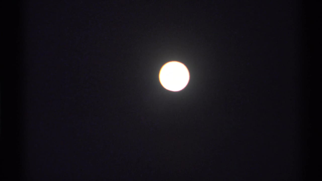 Overexposed moon near the top of a dark 8mm frame, with visible grain and slight haloing.