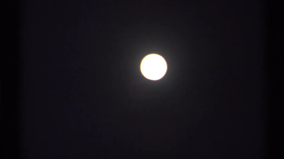 Overexposed moon near the top of a dark 8mm frame, with visible grain and slight haloing.