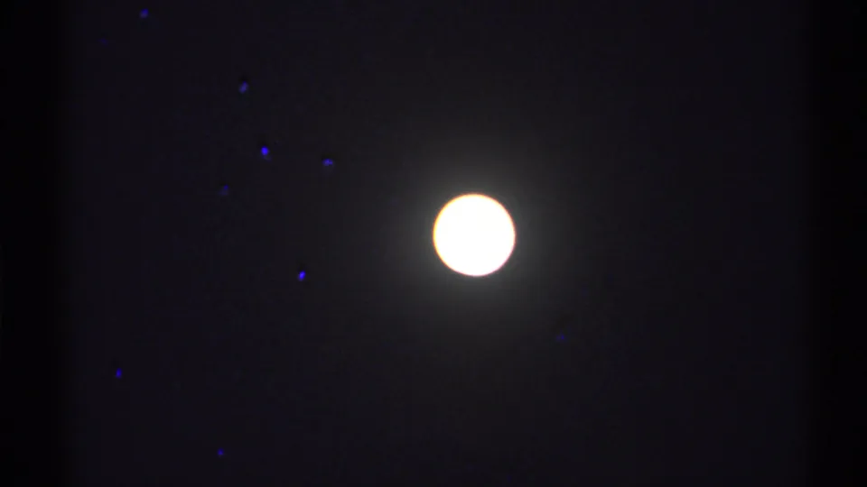 Glowing moon in a dark night sky, with visible 8mm grain and small colored specks in the frame.