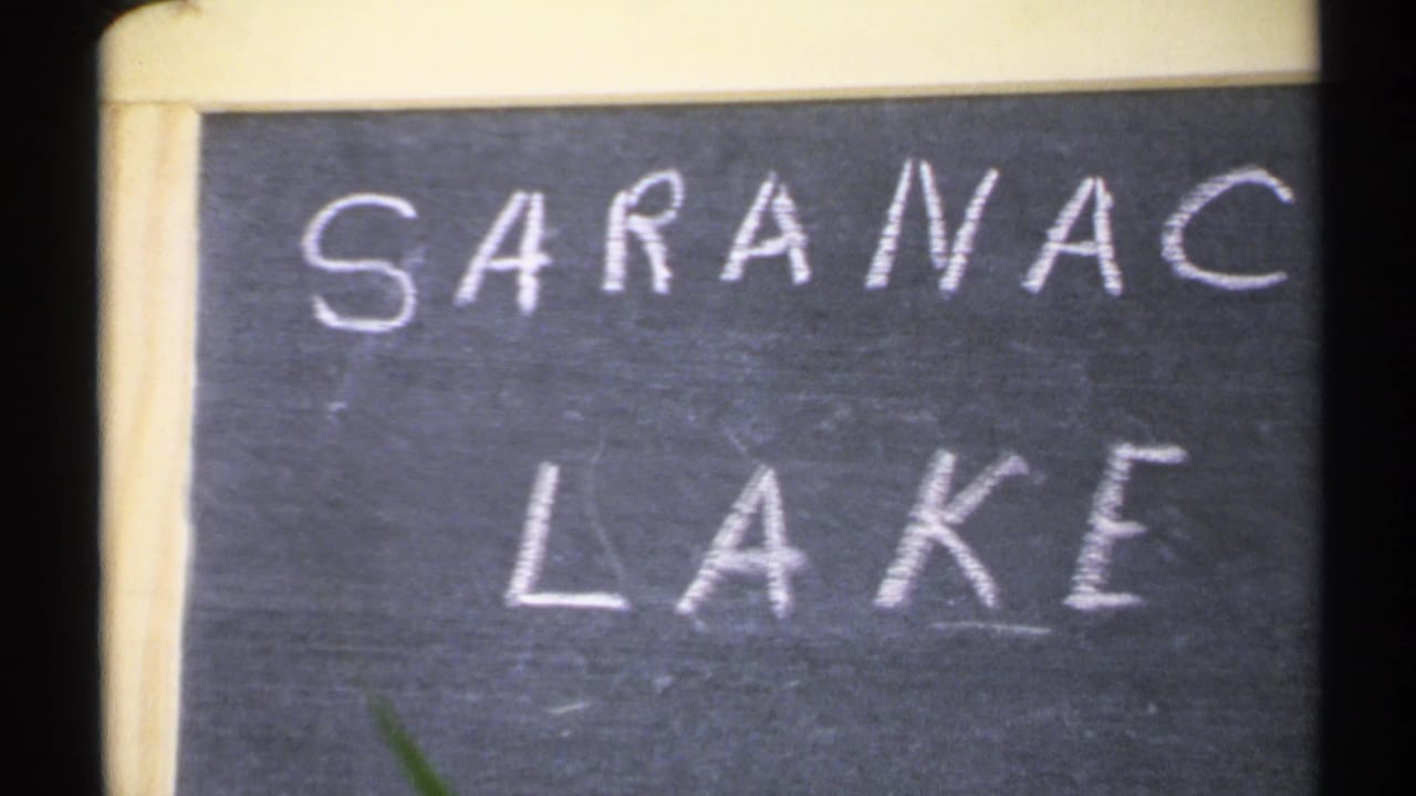 1971 New York 8mm frame with a hand-drawn Saranac Lake sign in white chalk, seen close and slightly cropped.