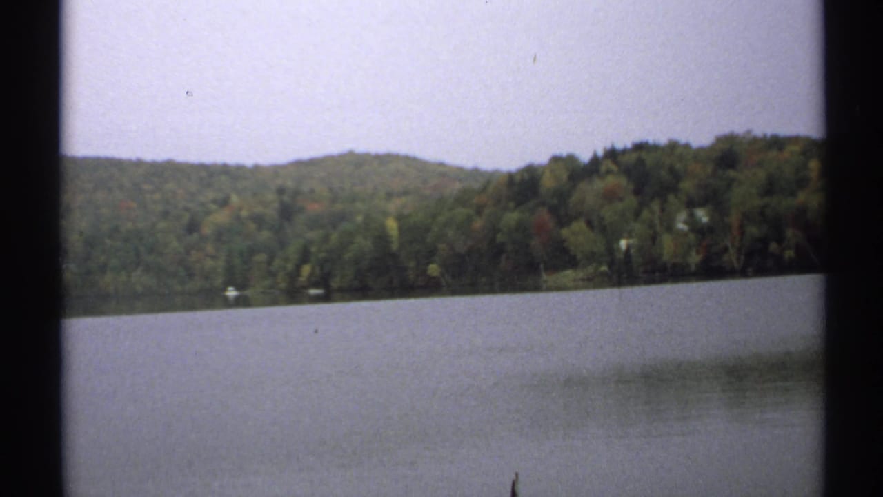 Calm lake below forested hills with pale sky and 8mm frame edges.