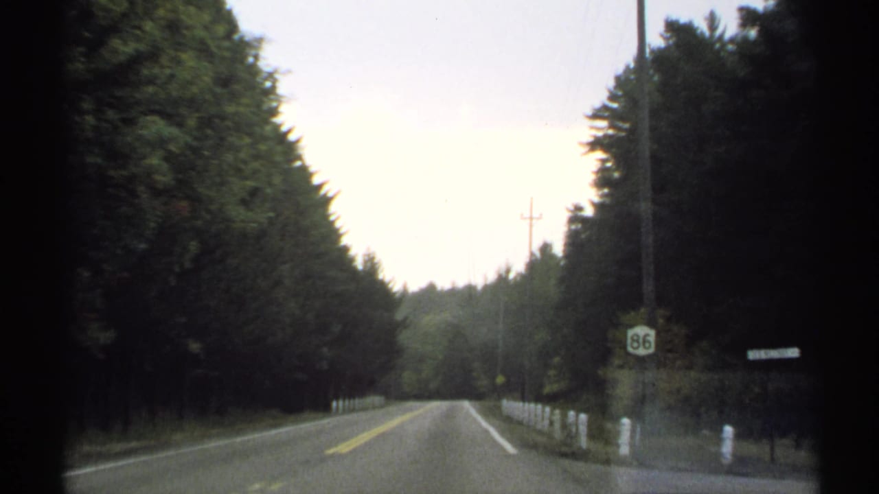 1971 New York road view from a car, showing a tree-lined two-lane road, white roadside posts, utility poles, and a Route 86 sign.