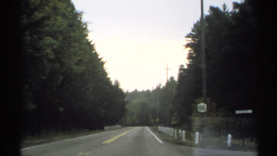 1971 New York road view from a car, showing a tree-lined two-lane road, white roadside posts, utility poles, and a Route 86 sign.