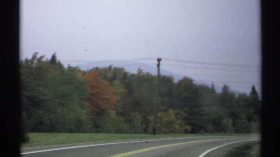 1971 8mm New York home-movie view of a curving rural road with trees, utility poles, power lines, and distant hazy hills.
