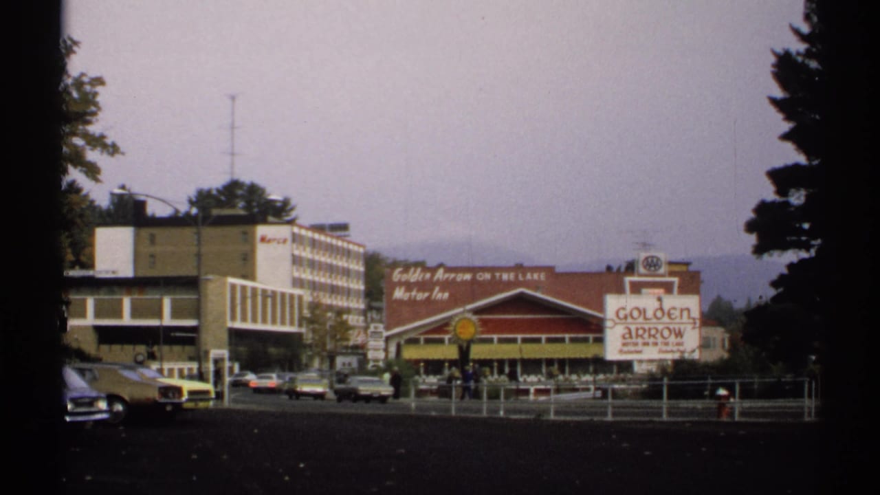 1971 Lake Placid view of Golden Arrow Motor Inn signage, a Shell sign, parked cars, and adjacent commercial buildings.