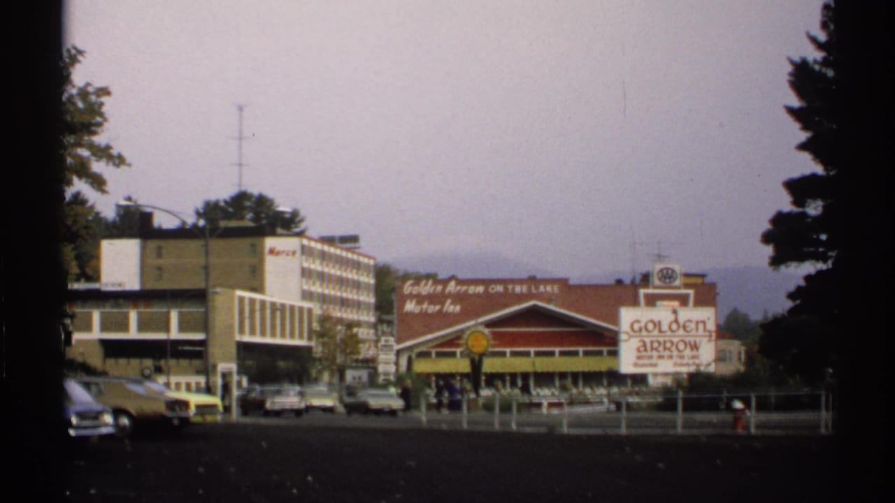 1971 New York 8mm view of the Golden Arrow Motor Inn area, with signage, parked vintage cars, and a roadside building.