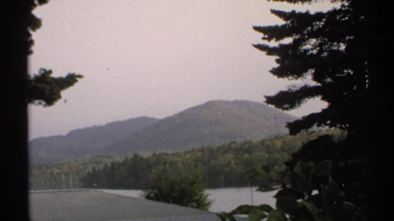 1971 New York 8mm scenic view of a lake, wooded hills, and pine branches under overcast light.
