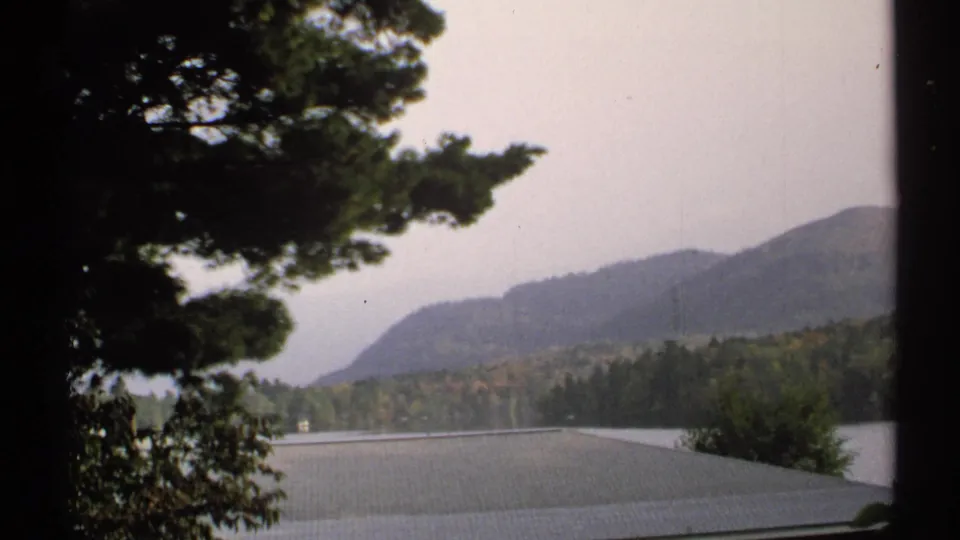 1971 New York 8mm view across water toward forested hills, with trees blocking part of the frame.