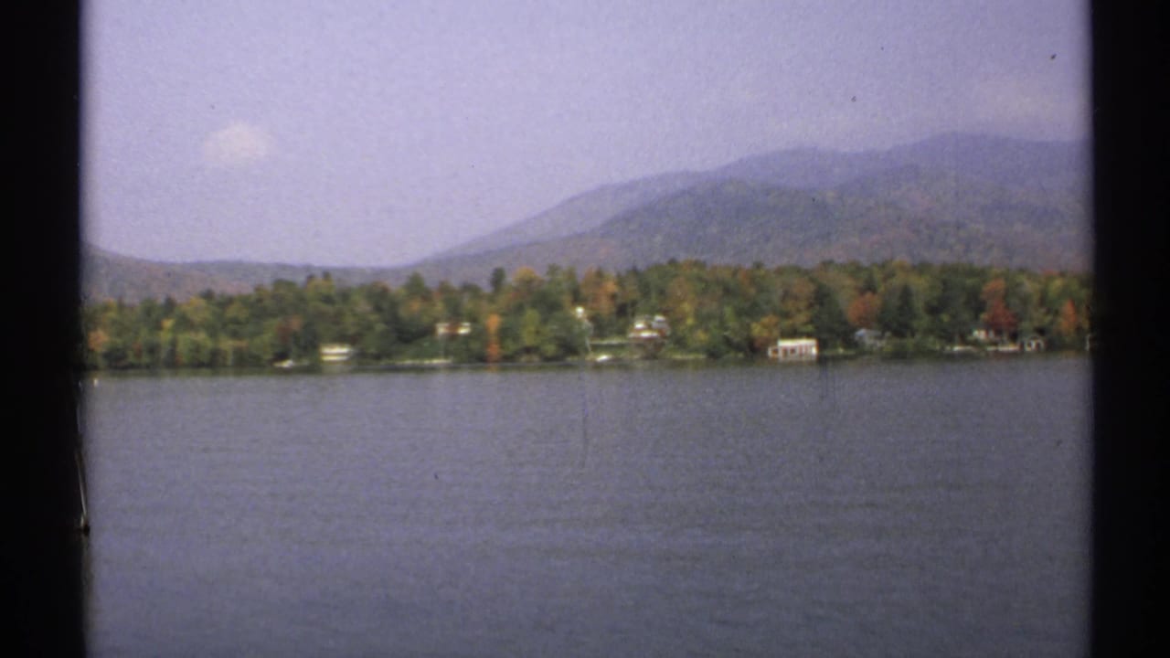 Calm lake with autumn shoreline trees and hazy mountains beyond.
