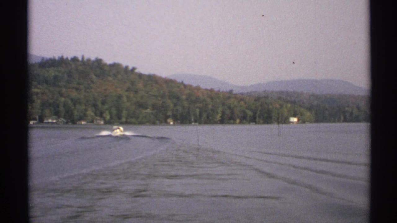 The 1971 8mm footage shows a motorboat pulling away across the lake, with wake lines leading back toward a wooded New York shoreline.