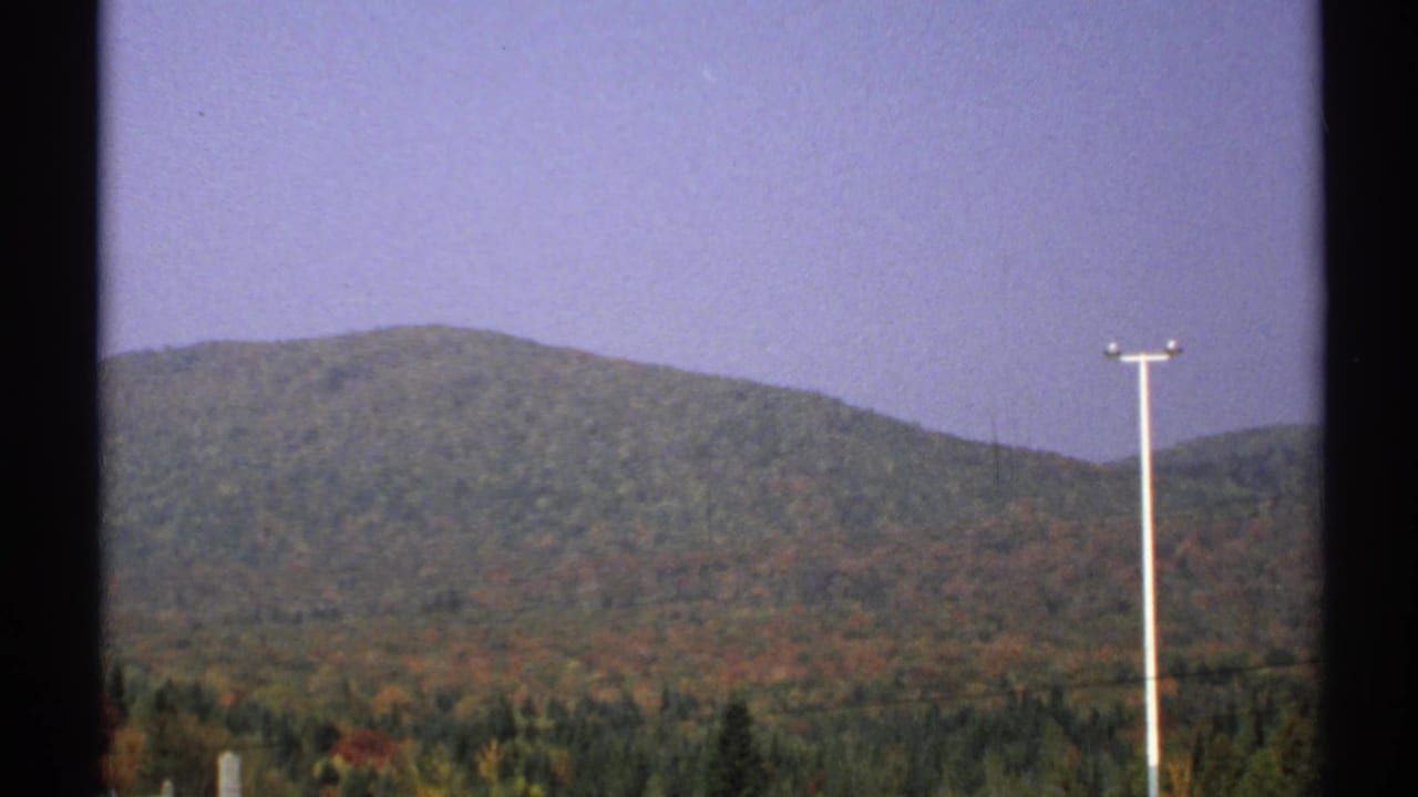 1971 New York 8mm frame with distant wooded hills, a band of autumn foliage, pale sky, and a tall utility pole in the foreground.